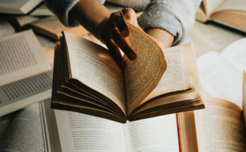 person holds a book over a stack and turns the page