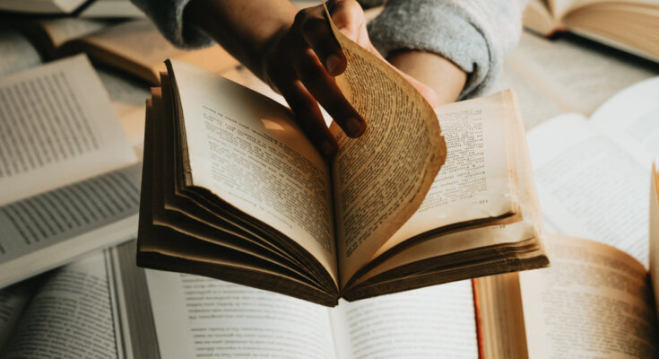 person holds a book over a stack and turns the page