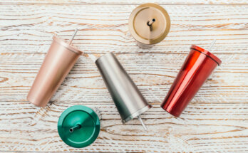 Four assorted colored tumblers sit on a wooden table, perfect for kids, alongside stainless steel Coke bottles for added appeal.